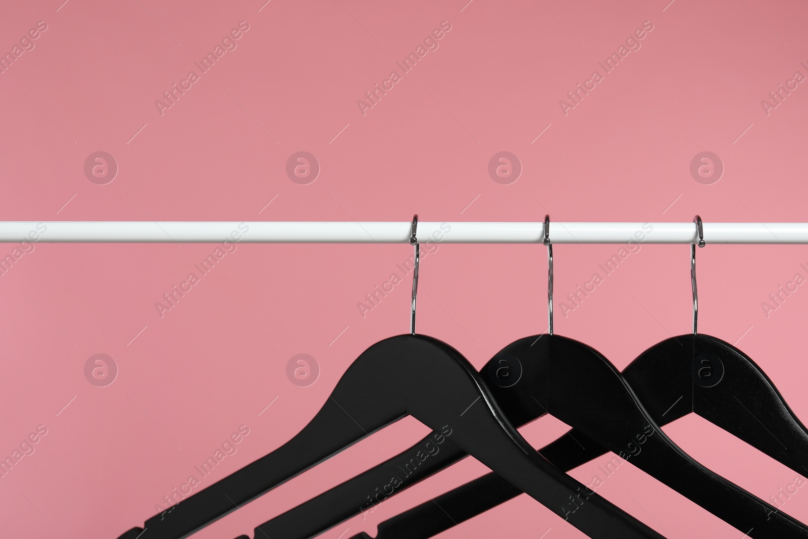 Photo of Black clothes hangers on rack against pink background. Space for text