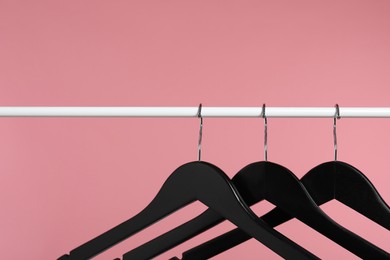 Photo of Black clothes hangers on rack against pink background. Space for text