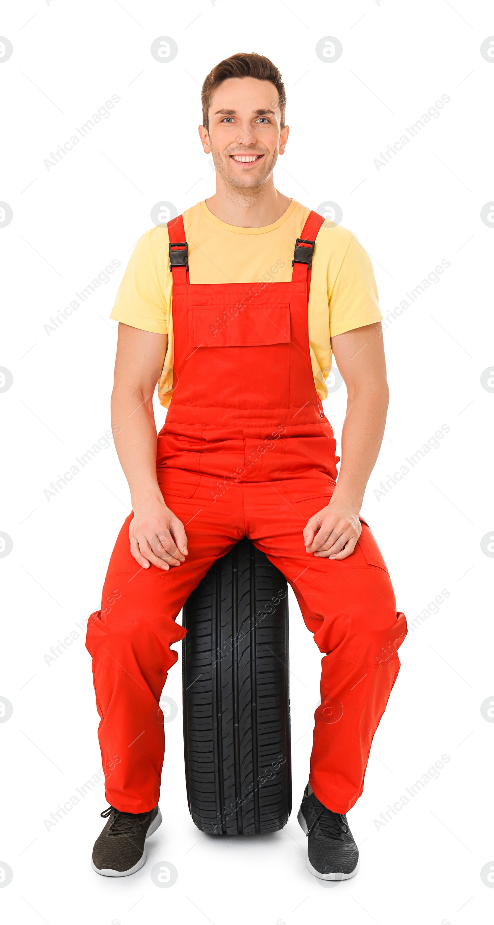 Photo of Young mechanic in uniform with car tire on white background