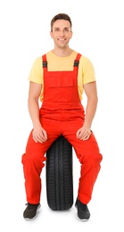 Photo of Young mechanic in uniform with car tire on white background