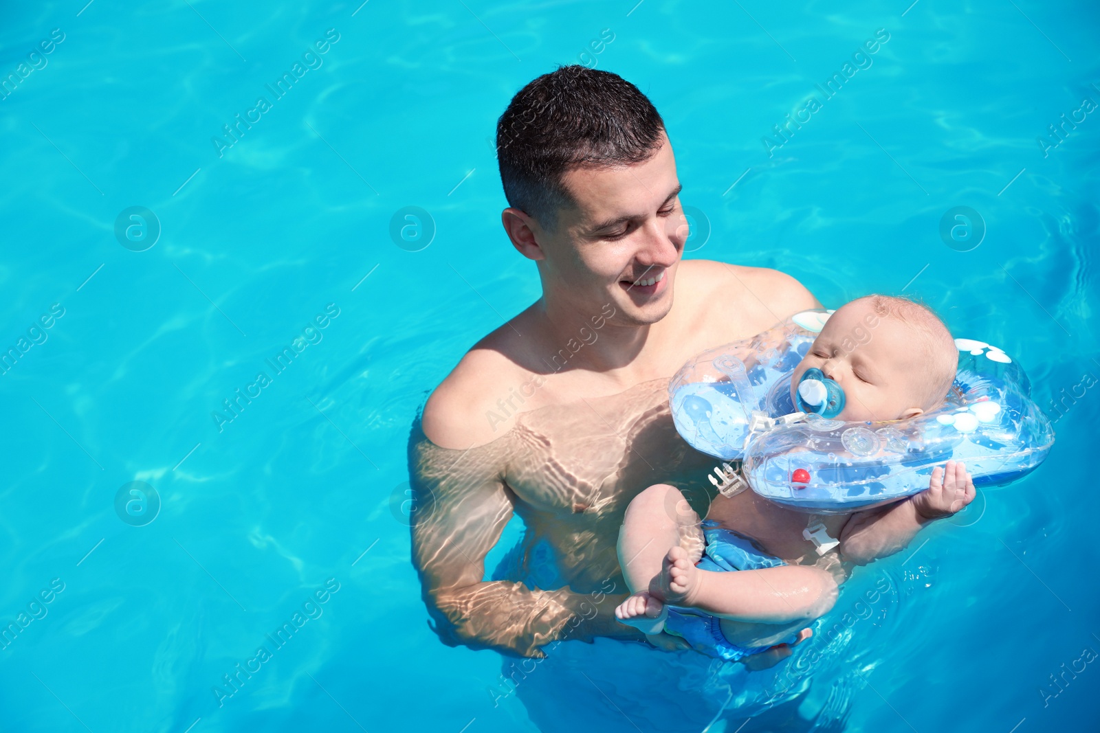 Photo of Man with his little baby in swimming pool on sunny day, outdoors