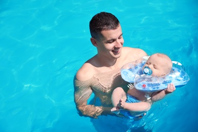 Man with his little baby in swimming pool on sunny day, outdoors