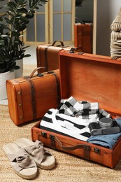 Photo of Open suitcase with folded clothes, accessories and shoes on floor in room