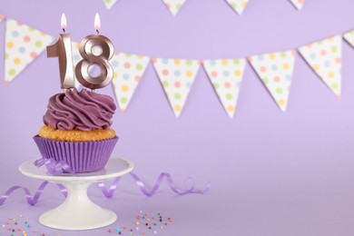 Photo of Coming of age party - 18th birthday. Delicious cupcake with number shaped candles on violet background, space for text