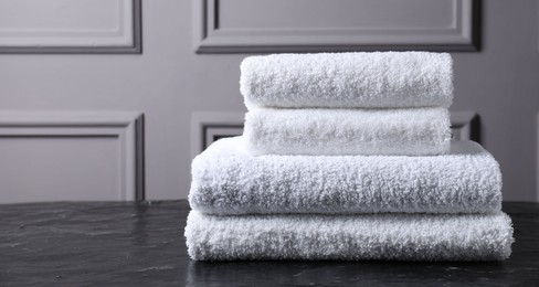 Photo of Stacked terry towels on black textured table indoors, space for text