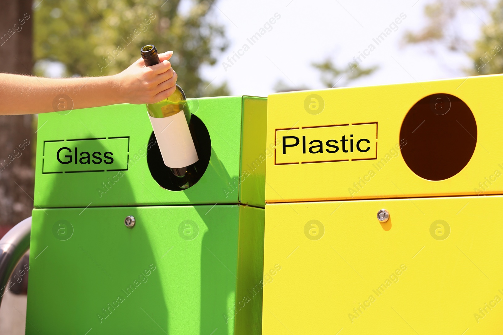 Photo of Woman throwing glass bottle into sorting bin on city street, closeup. Recycling waste