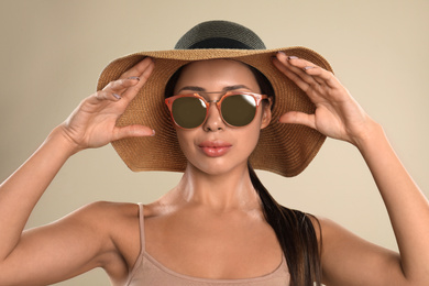 Beautiful young woman wearing sunglasses and hat on beige background