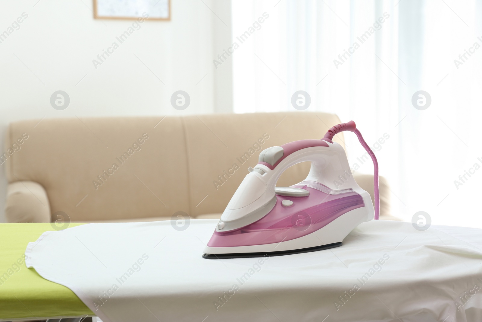 Photo of Board with modern iron and shirt at home. Laundry day