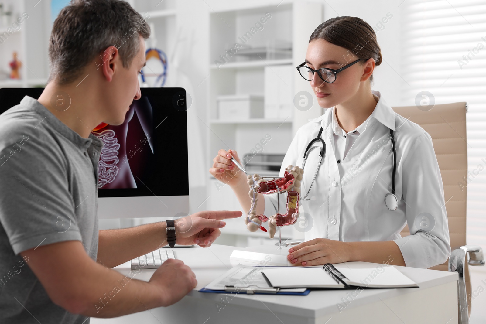 Photo of Gastroenterologist with anatomical model of large intestine consulting patient at table in clinic