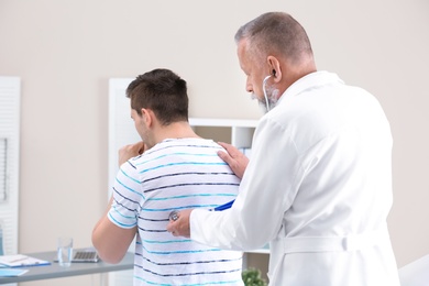 Doctor examining coughing young man at clinic