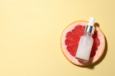 Photo of Bottle of cosmetic serum and grapefruit slice on wet yellow background, top view. Space for text