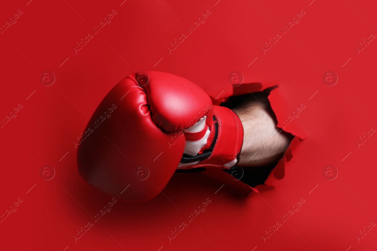 Photo of Man breaking through red paper with boxing glove, closeup