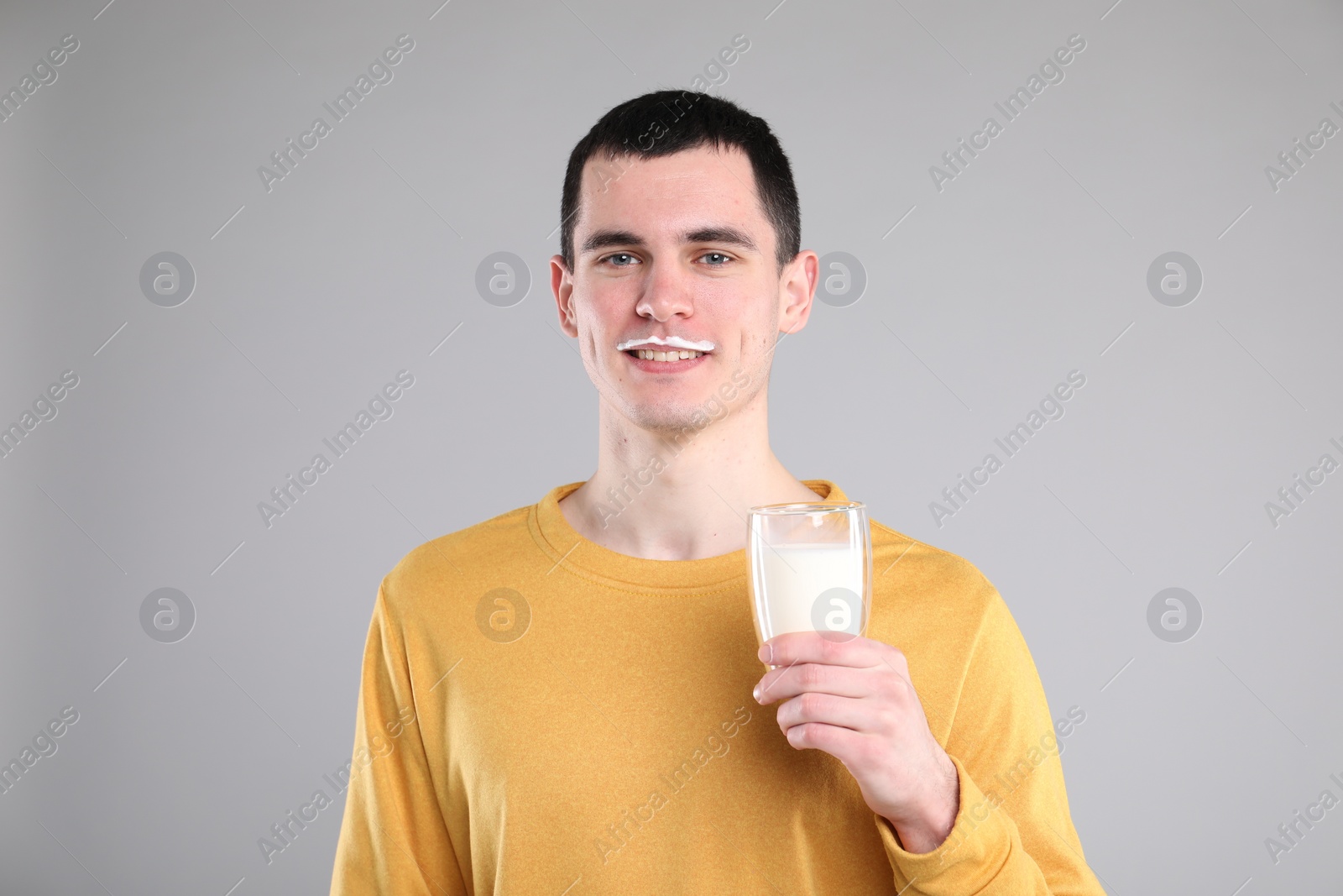 Photo of Happy man with milk mustache holding glass of tasty dairy drink on gray background