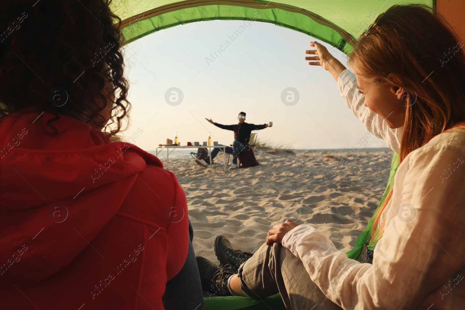 Photo of Friends resting on sandy beach. View from camping tent