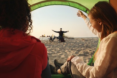 Photo of Friends resting on sandy beach. View from camping tent
