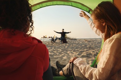 Friends resting on sandy beach. View from camping tent