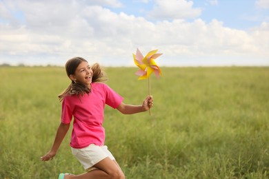 Photo of Cute little girl with pinwheel in field, space for text. Child spending time in nature