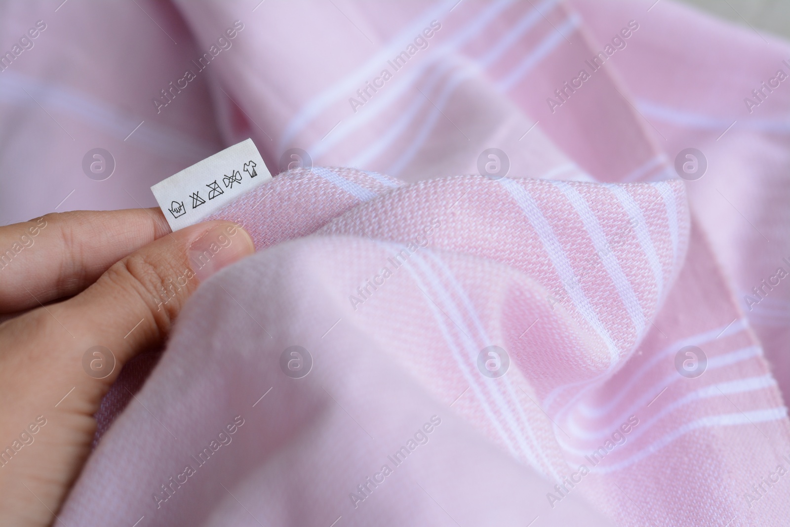 Photo of Woman holding white clothing label on pale pink garment, closeup