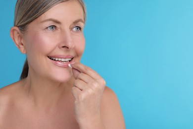 Photo of Beautiful woman taking vitamin pill on light blue background, space for text