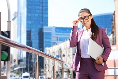 Photo of Beautiful businesswoman with laptop in city on sunny day