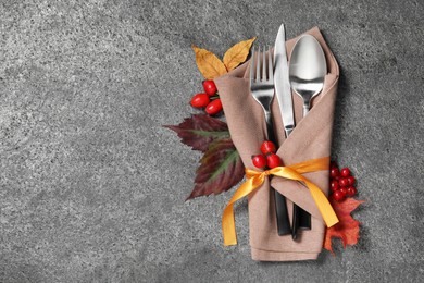 Photo of Thanksgiving table setting. Cutlery, napkin, autumn leaves and berries on grey background, flat lay with space for text