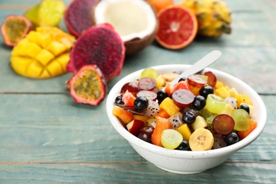 Photo of Delicious exotic fruit salad and ingredients on light blue wooden table