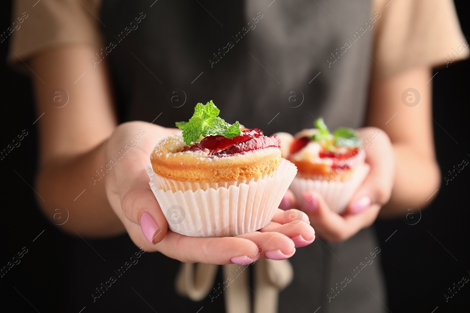 Photo of Woman with delicious plum cupcakes on black background, closeup