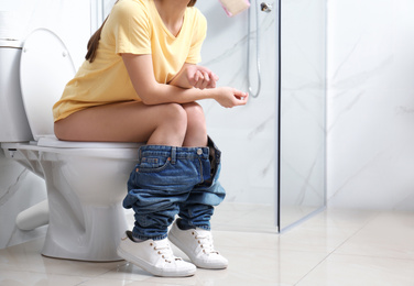 Photo of Woman sitting on toilet bowl in bathroom, closeup