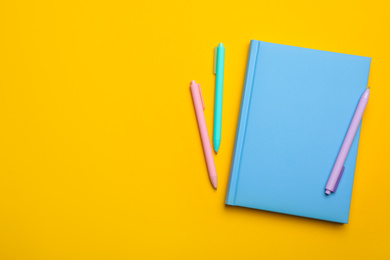Photo of Light blue notebook and pens on yellow background, flat lay. Space for text