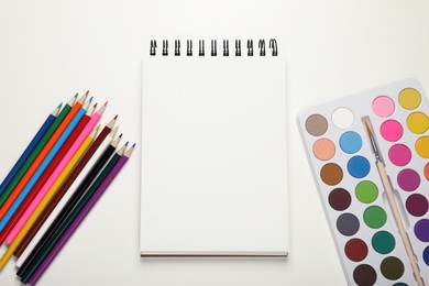 Watercolor palette, empty notebook and colorful pencils on white background, flat lay. Space for text