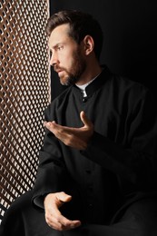 Catholic priest in cassock talking to parishioner in confessional