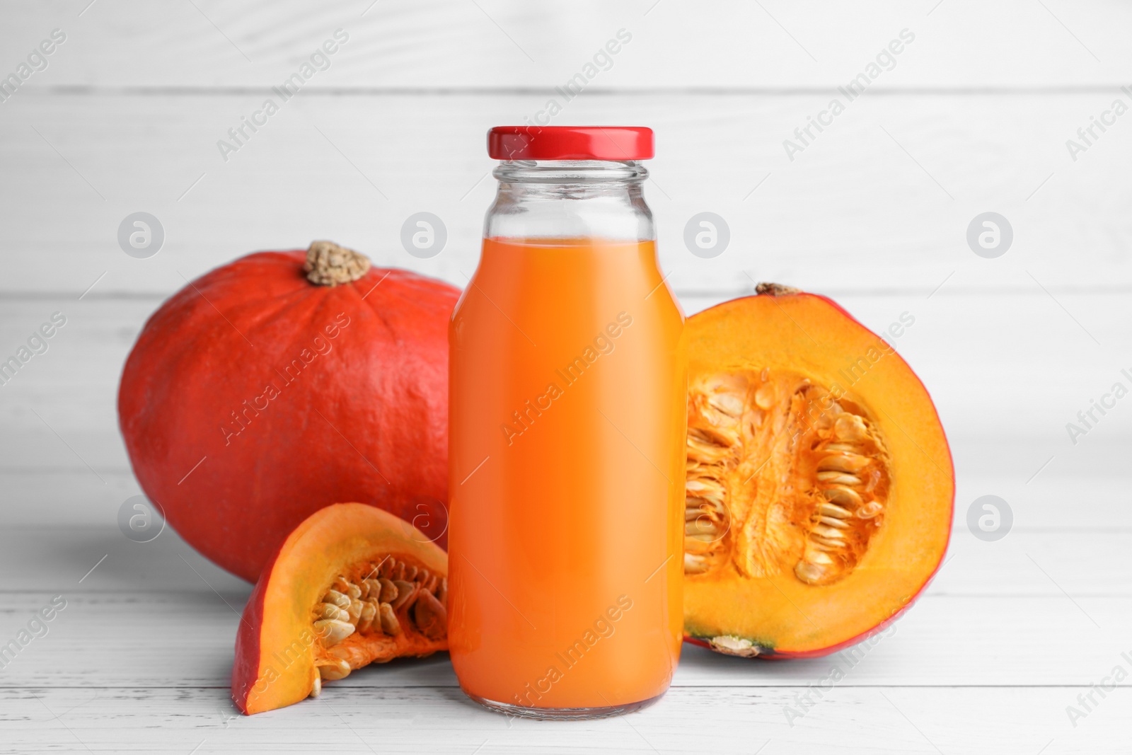 Photo of Tasty pumpkin juice in glass bottle, whole and cut pumpkins on white wooden table