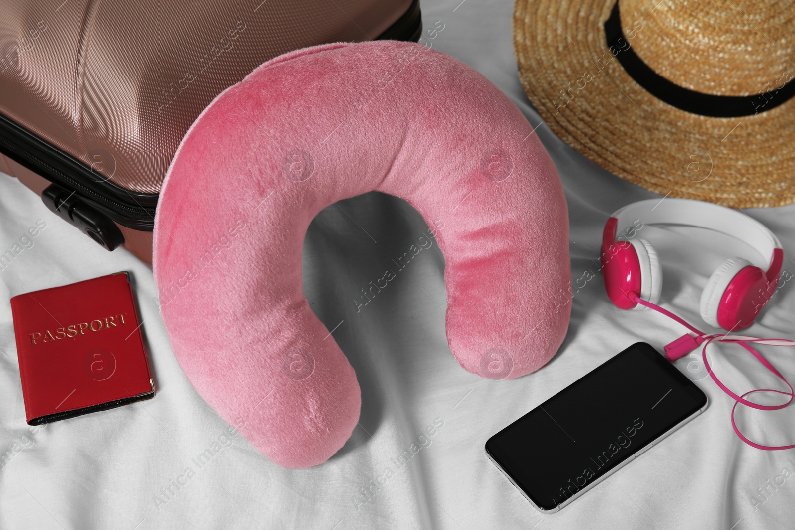 Photo of Pink travel pillow, suitcase, smartphone with headphones and passport on bed