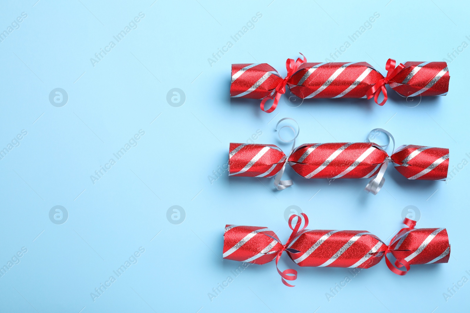 Photo of Red Christmas crackers on light blue background, flat lay. Space for text