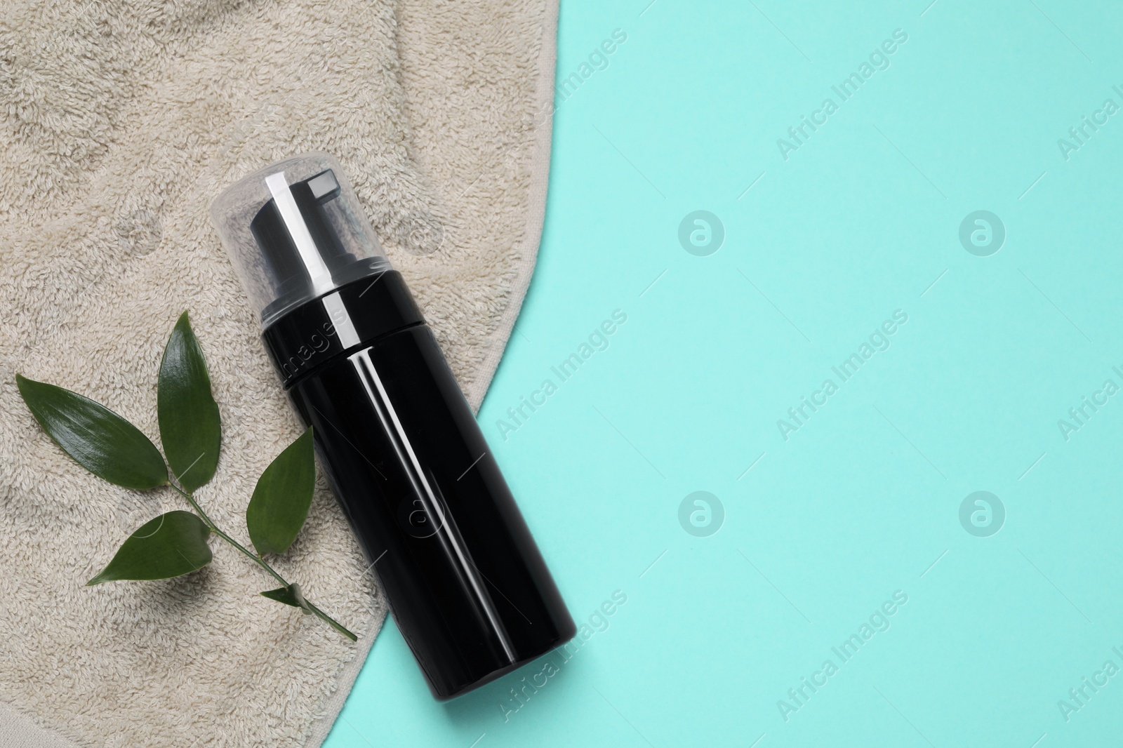 Photo of Bottle of face cleansing product, towel and leaves on turquoise background, flat lay. Space for text