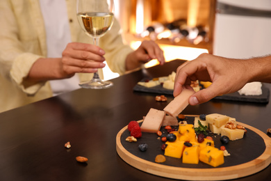 Couple with different types of delicious cheeses at table indoors, closeup