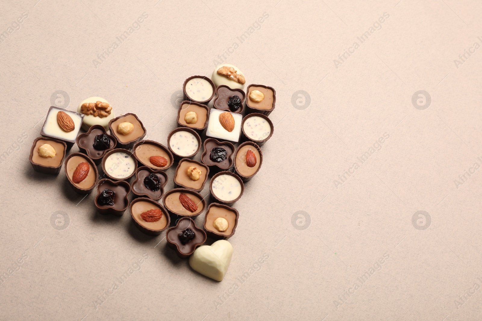 Photo of Heart made with delicious chocolate candies on beige background, above view. Space for text