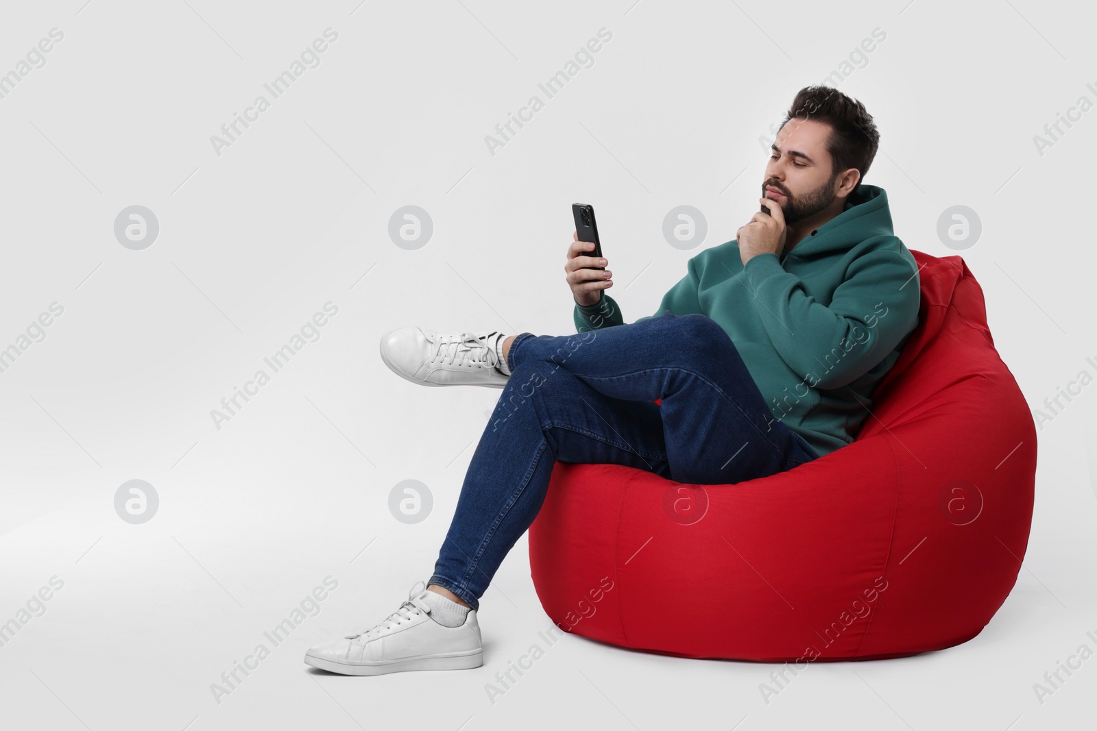 Photo of Handsome young man using smartphone on bean bag chair against white background, space for text