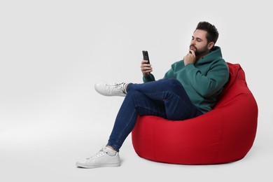 Handsome young man using smartphone on bean bag chair against white background, space for text