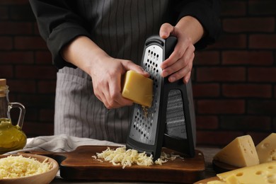 Woman grating cheese at wooden table, closeup