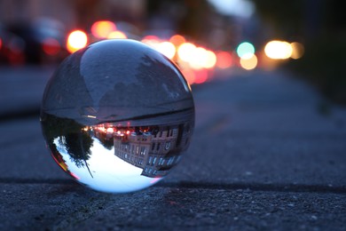 Photo of Beautiful city street, overturned reflection. Crystal ball on asphalt road outdoors, closeup. Space for text