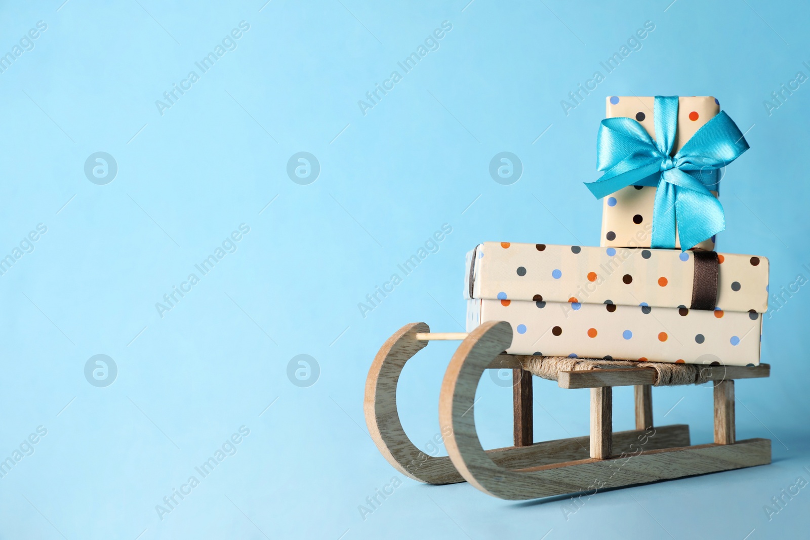 Photo of Wooden sleigh with Christmas gift boxes on light blue background, space for text