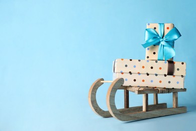 Photo of Wooden sleigh with Christmas gift boxes on light blue background, space for text