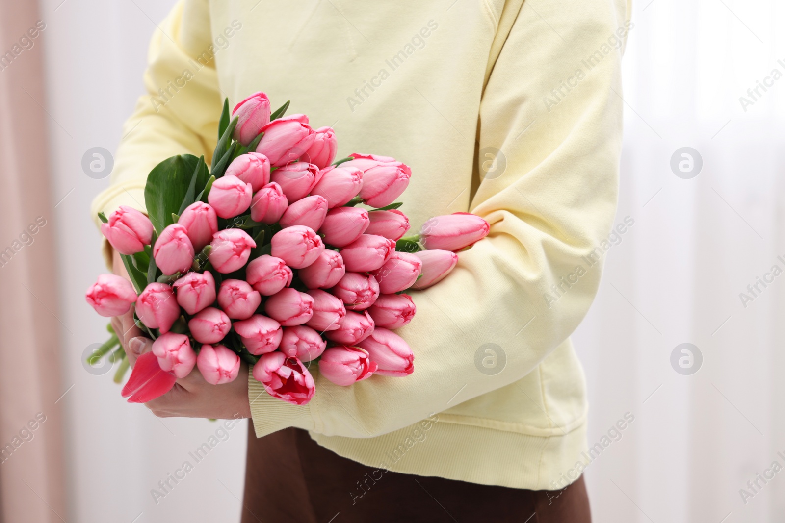 Photo of Woman holding bouquet of pink tulips indoors, closeup