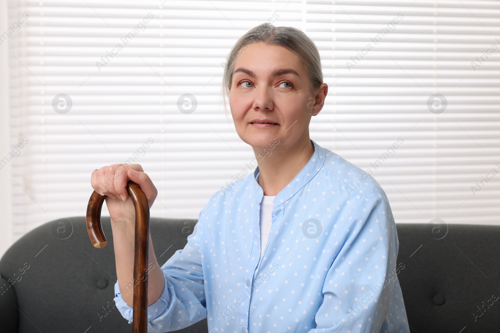 Photo of Senior woman with walking cane sitting on sofa at home