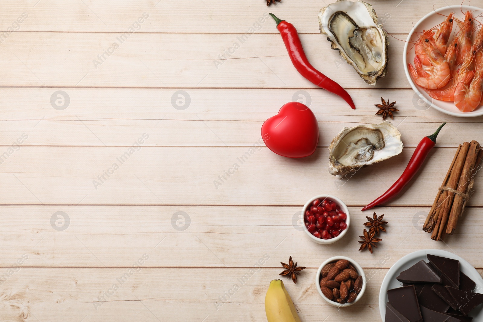 Photo of Natural aphrodisiac. Different food products and red decorative heart on light wooden table, flat lay. Space for text