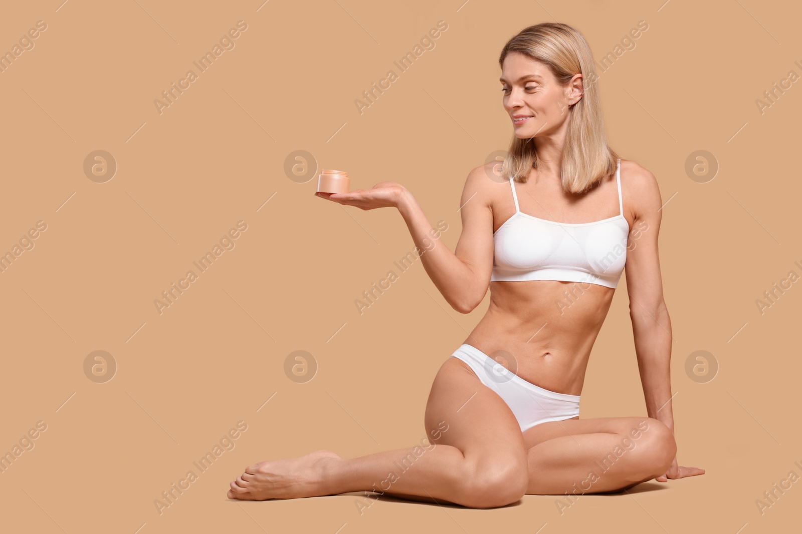 Photo of Woman with jar of body cream on beige background, space for text