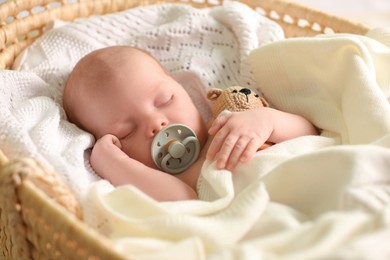 Cute newborn baby sleeping on white blanket in wicker crib, closeup