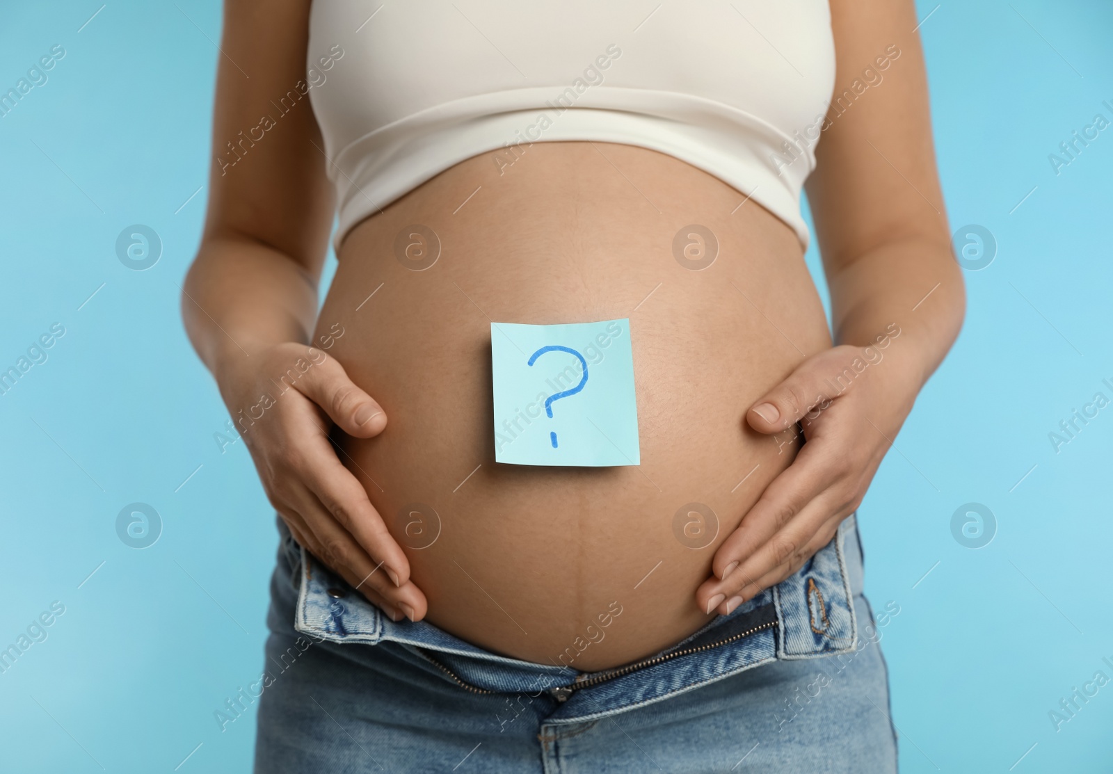 Photo of Pregnant woman with sticky note on belly against light blue background, closeup. Choosing baby name