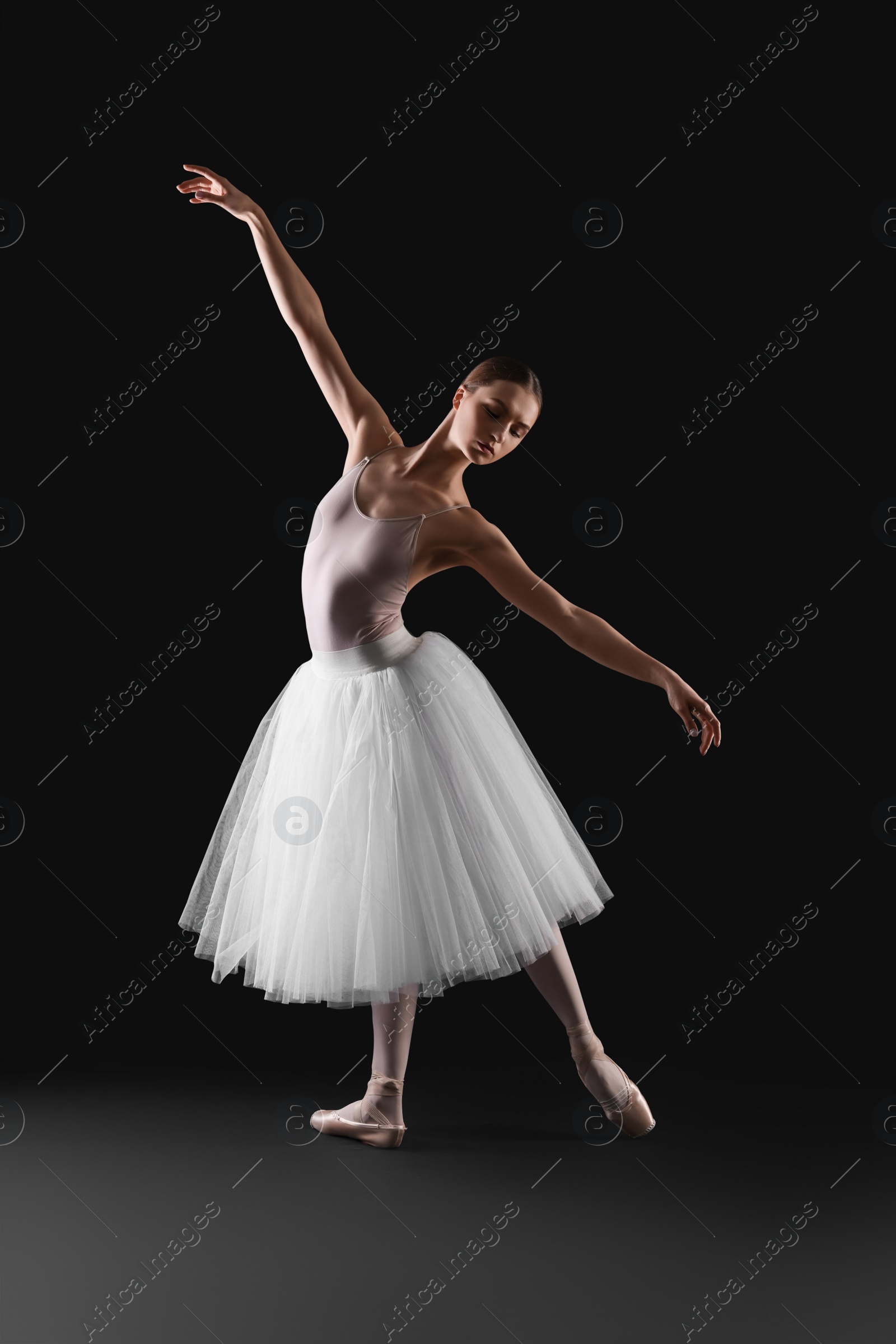 Photo of Young ballerina practicing dance moves on black background